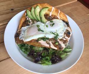 A fried tortilla bowl filled with beef chili and topped with over easy eggs, cheddar cheese, and avocado